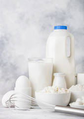 Fresh dairy products on white table background. Plastic bottle and glass of milk, bowl of cottage cheese and baking flour and mozzarella. Eggs and cheese. Steel whisk.