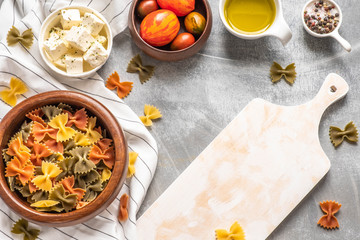 Pasta food cooking concept. Ingredients for preparation pasta - tomato, olive oil, spices, olives, tomato, grey wooden background. Top view with copy space for text.