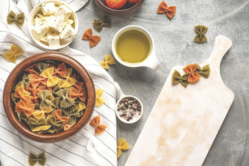 Pasta food cooking concept. Ingredients for preparation pasta - tomato, olive oil, spices, olives, tomato, grey wooden background. Top view with copy space for text.