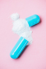 close-up shot of broken medical capsule  with spilled powder on pink