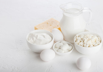 Fresh dairy products on white table background. Glass jar of milk, bowl of sour cream and cottage cheese and mozzarella. Eggs in and cheese. Space for text