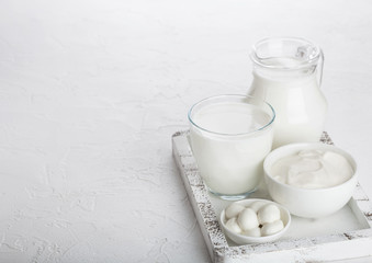 Fresh dairy products in vintage wooden box on white table background. Jar and glass of milk, bowl of sour cream and mozzarella cheese. Space for text