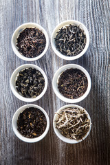 closeup top view on assorted tea leaves in six white small round vessels