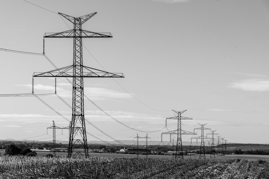 Line of transmission towers, or electricity pylons, in the rural landscape. Black and white image.