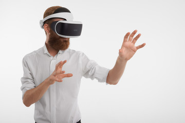 Isolated studio shot of modern unshaven European businessman using 3d VR headset feeling mighty, reaching out hands as of interacting with something invisible, playing video games in his office - Powered by Adobe