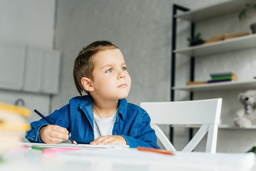 thoughtful little kid drawing with color pencils at home
