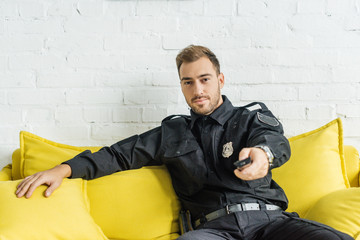 handsome young policeman sitting on couch and using tv remote control