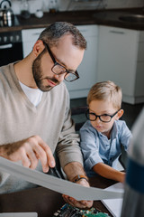 father and son in glasses modeling rocket and looking at blueprint at home