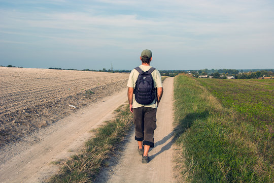Man traveler with a backpack walking along a dirt road