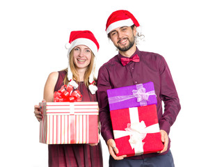 Happy couple of young people in Santa Claus hats and with boxes of gifts in their hands on a light background. Man and woman in a festive mood - New Year, Christmas, shopping for gifts.