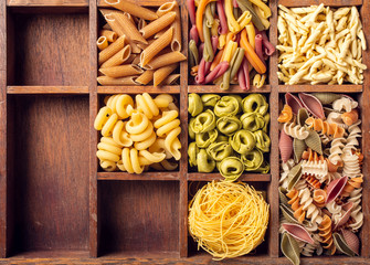 Assorted colorful italian pasta in wooden box. Healthy food background concept. Flat lay, top view. Copy space.