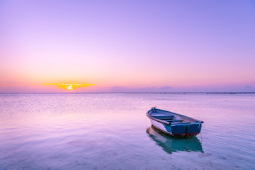 Mauritius Boat in the sea with pink and purple colors during Sunset in beautiful Mauritius paradise landscape. Mauritius nature view of colorful sky and light of sun. Reflection on the sea near beach