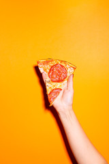 Hand holding slice of pizza isolated on bright orange background.