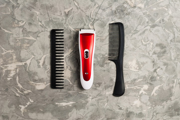 One red and white professional clipper and two black plastic combs on old gray concrete surface. Top view