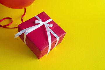 Red gift box with red balloon on yellow background. Copy space.