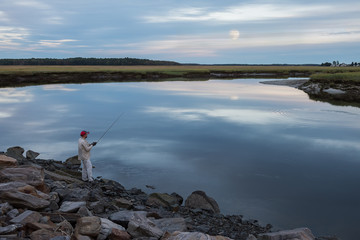 Fototapeta na wymiar Fisherman catches fish on the evening lake. USA. Maine. Portland. Beautiful sunset landscape of a calm lake. 