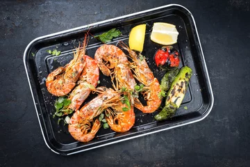 Foto op Plexiglas Traditional fried black tiger prawn with vegetable and lemon as top view on a black skillet © HLPhoto