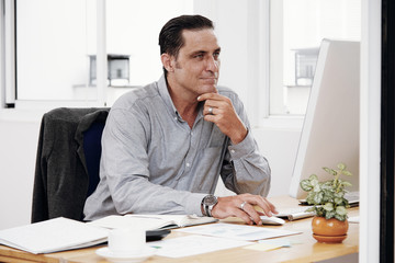 Mature businessman sitting at his workplace and looking at computer screen at office