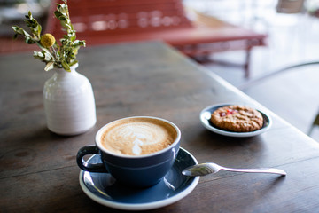 Beautiful stylish cup of coffee, as well as delicious cookies and a romantic bouquet of flowers on the background of a wooden table in a bright and cozy cafe