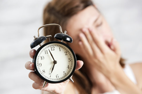 Sleepy tired woman holding alarm clock, seven o'clock in the morning, not an early bird concept