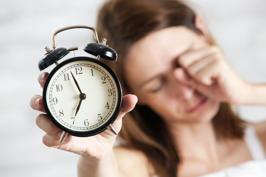 Sleepy tired woman holding alarm clock, seven o'clock in the morning, not an early bird concept