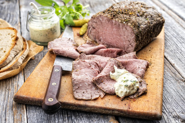 Traditional lunch meat with sliced cold cuts roast beef, remoulade and farmhouse bread as closeup on a cutting board