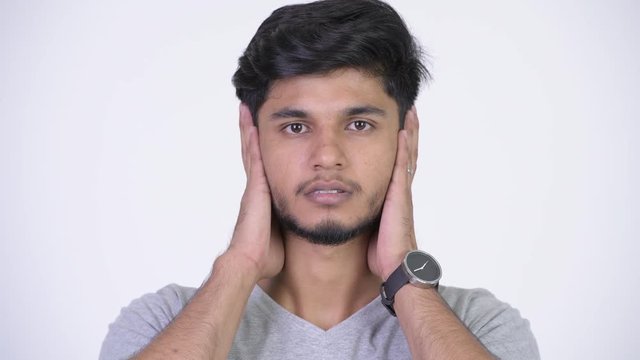 Young handsome bearded Indian man covering ears as three wise monkeys concept