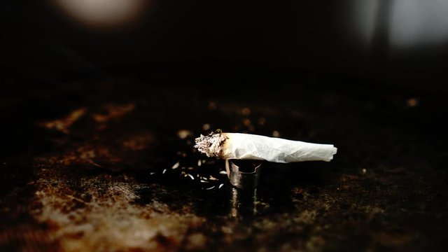 Rolled smoking item as in cigarette or cannabis joint burning down to ashes in a time lapse indoors isolated on metal plate