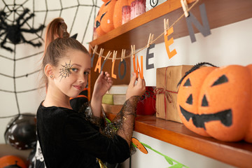Pretty Caucasian girl in Halloween costume with face painting looking at camera while standing in beautifully decorated bedroom