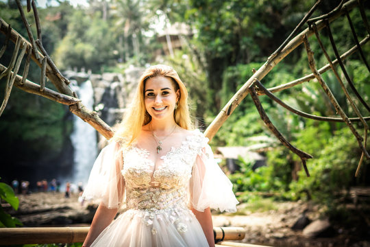 Happy young woman bride in wedding white dress smiling on a waterfall background. Bali island.