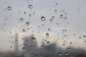 Rain water drops on window glass and silhouette of city