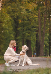 Beautiful young woman walks with her retriever in the park in autumn.