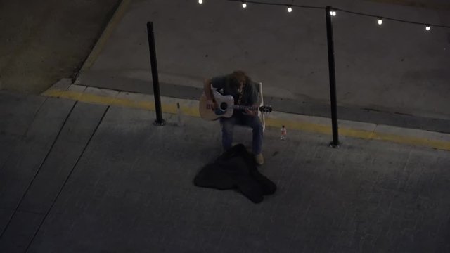 Street busker playing guitar downtown neon reflections on instrument