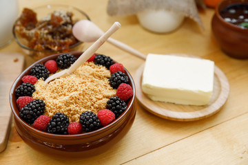 Porridge with berries and butter in wooden dishes with cutlery on a wooden table