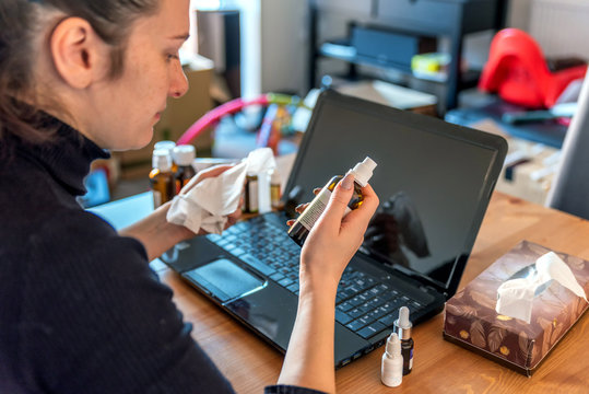 young sick woman working from home on laptop next to medicines