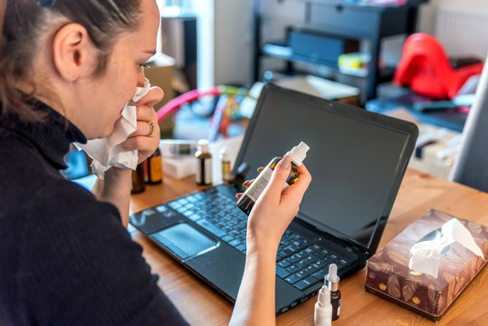 young sick woman working from home on laptop next to medicines