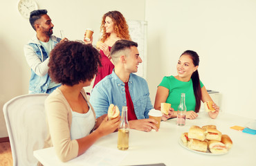 corporate, celebration and people concept - happy friends or team eating sandwiches with coffee and non-alcoholic drinks at office