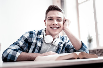 Happy smile. Positive emotional student leaning to the table and smiling while sitting with the book and getting ready for his exam