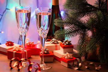 Two glasses of champagne, a Christmas tree and many small gift boxes. In the background a garland in blur.