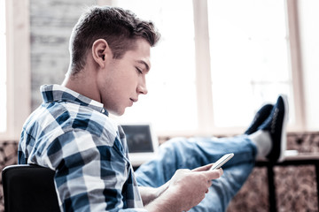 Reading messages. Concentrated young man thoughtfully looking at the screen of his smartphone while reading messages
