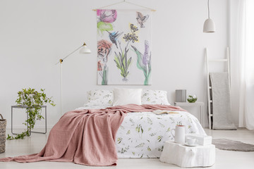Peach blanket and white with green pattern linen on bed in a natural bright bedroom interior. Tapestry with colorful flowers and birds on the back wall. Real photo. - obrazy, fototapety, plakaty