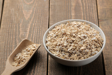 Dry oatmeal in a white bowl and a wooden spoon. food. healthy food. on a brown wooden table.