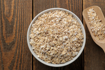 Dry oatmeal in a white bowl and a wooden spoon. food. healthy food. on a brown wooden table.