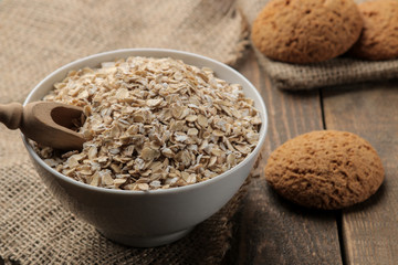 Dry oatmeal and oatmeal cookies in a white bowl and a wooden spoon. food. healthy food. on a brown wooden table.