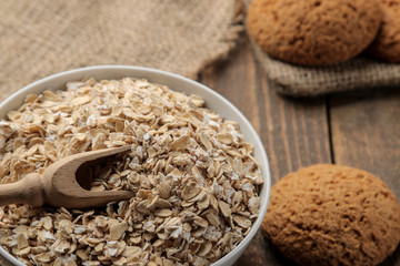 Dry oatmeal and oatmeal cookies in a white bowl and a wooden spoon. food. healthy food. on a brown wooden table.