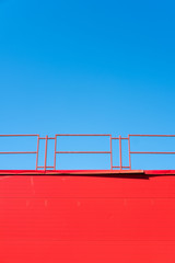 Red on blue. Red wall with a fence against the blue sky