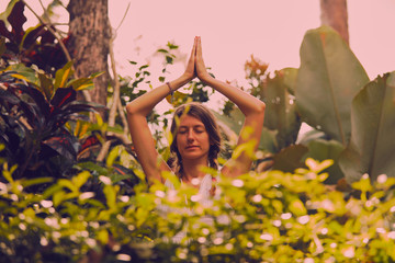 Young woman practicing yoga - meditation in the tropical garden.