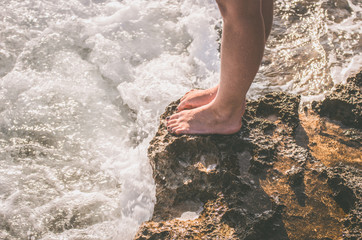 Naked female legs on a rocky cliff washed by sea foam
