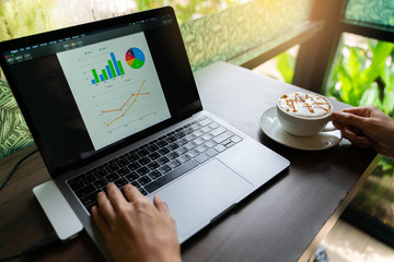 Young Business working create chart on laptop and drink hot Caramel coffee