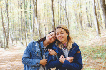 Two young girl friends walking in autumn forest. Girlfriends hiking in the fall.